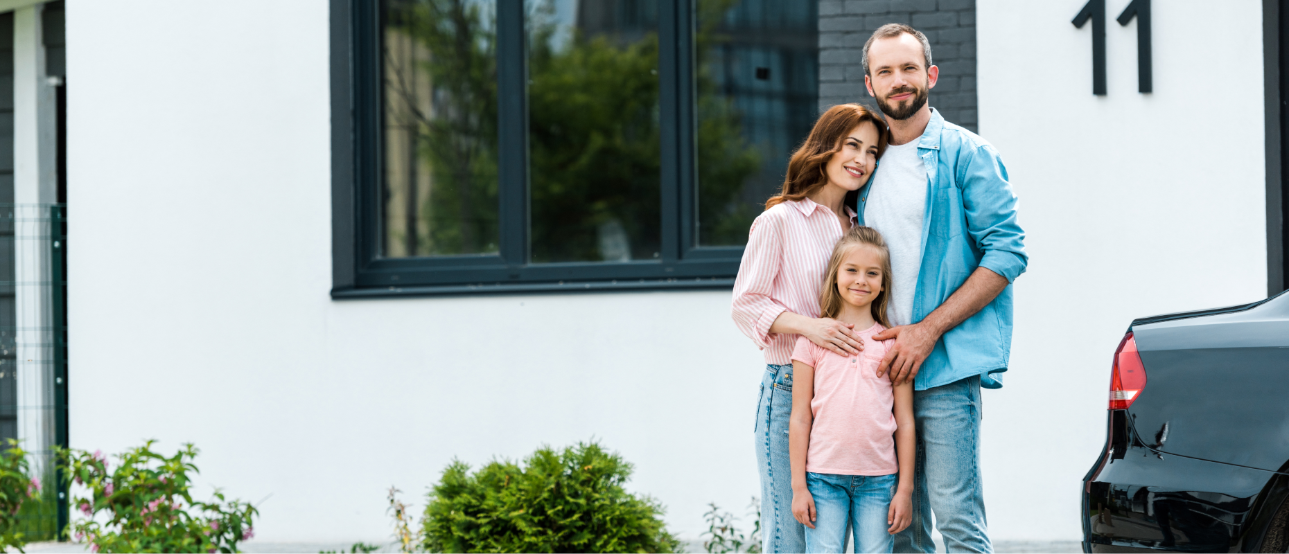 Happy family of three standing outside their new home purchased with Key Mortgages support.
