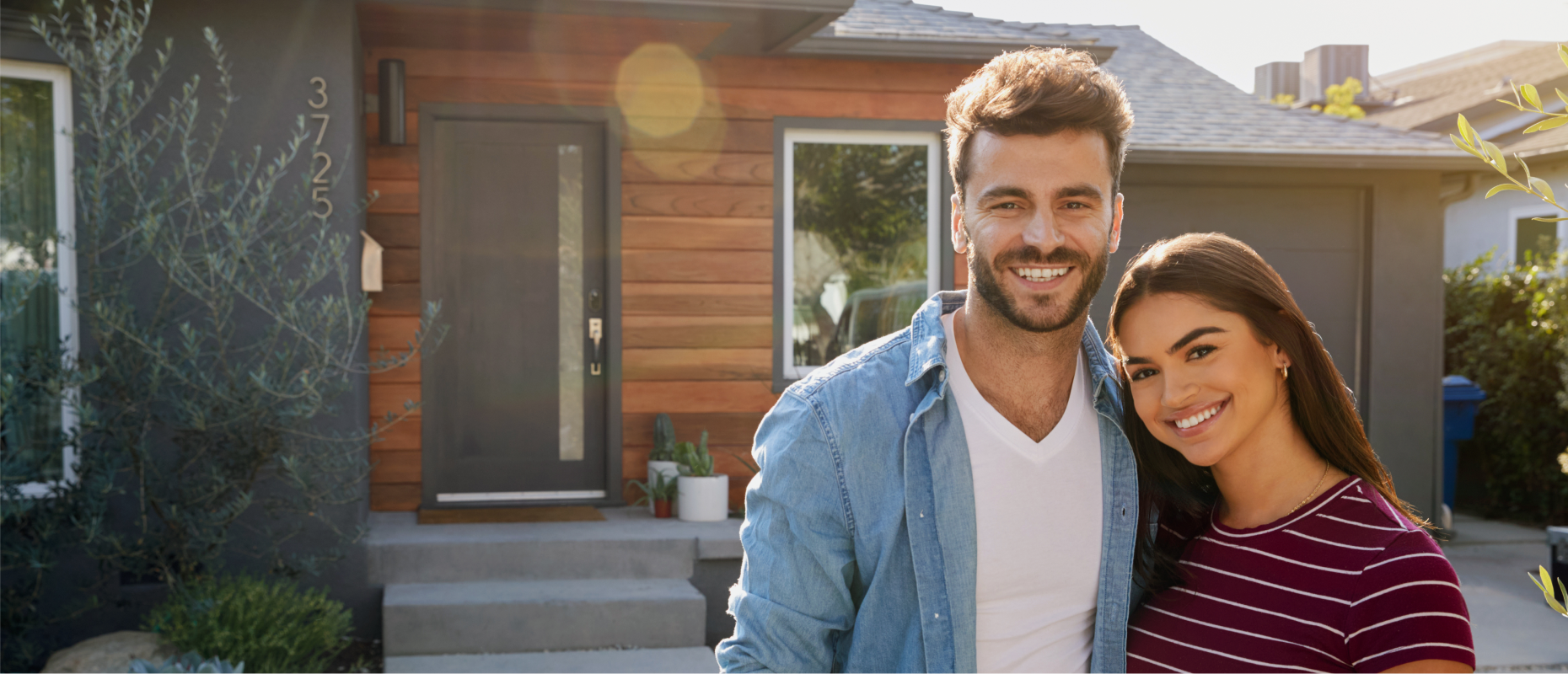 Smiling young couple standing in front of their new home financed through Key Mortgages.